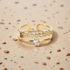 The golden double-layered ring features multiple round transparent gemstones on the upper layer and a large round transparent gemstone in the center on the lower layer. It has a white stone countertop details Picture